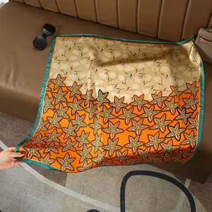 Macro detail of large square silk scarf with orange floral pattern on leather sofa