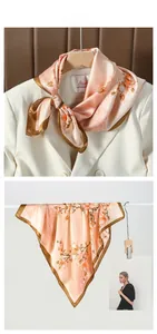 Détail macro du foulard carré en satin rose pêche fleuri sur un blazer blanc