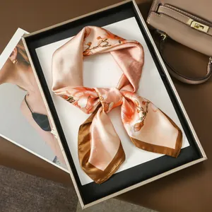 Élégant foulard en soie rose et or avec motif floral présenté sur un plateau blanc