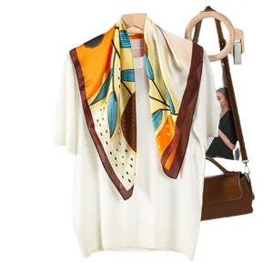 Silk-like square scarf with vibrant botanical patterns worn with a knit top and handbag