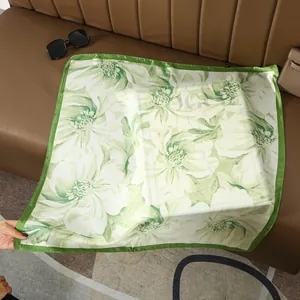 Detailed view of a green floral silk scarf styled with sunglasses on a leather sofa