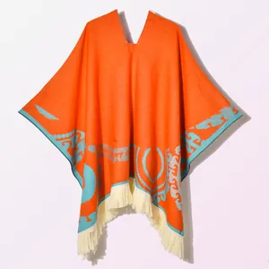 Close-up of orange knitted shawl featuring blue ethnic patterns and cream fringe details