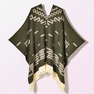 Detail of V-neck dark green knit poncho featuring white geometric jacquard and thick fringes