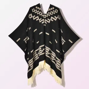 Close-up of black knitted poncho featuring white geometric jacquard patterns and tassels