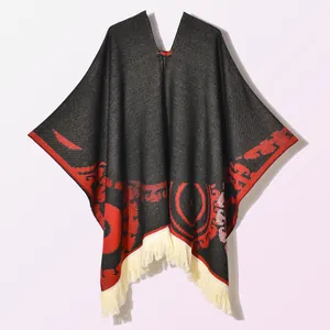 Close-up of knitted poncho featuring black ethnic patterns and cream fringe details
