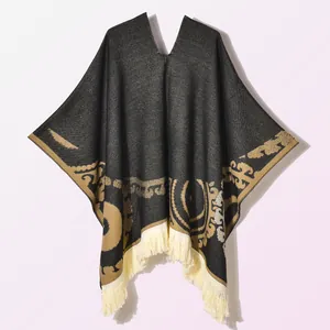 Detail of vintage golden jacquard patterns and cream fringe on a black poncho cloak