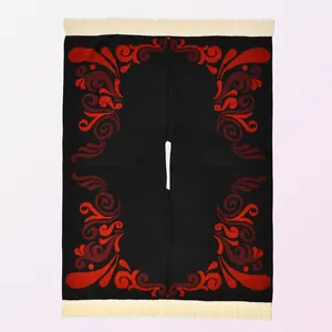 Detail of red vortex patterns and cream tassels on a black winter knitted poncho shawl