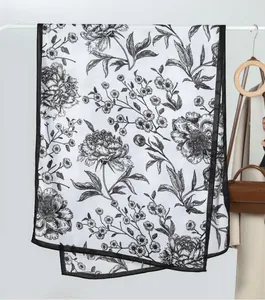 Detail eines weißen Samtschals mit elegantem schwarzen Pfingstrosenmuster und Saumkante