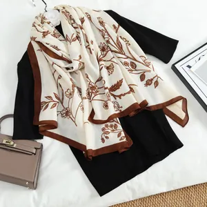 Detail of cream scarf with brown floral print draped over black knitwear and Kelly bag