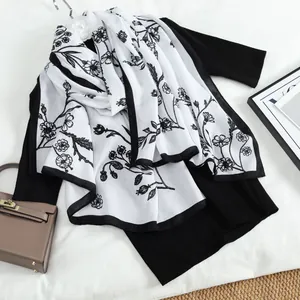 Close-up of elegant black and white floral print silk scarf on a black knit top