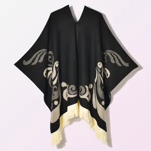 Detailed close-up of a black knit poncho featuring white jacquard patterns and long tassels