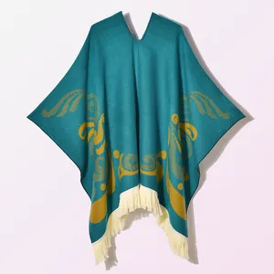 Detailed knit texture of a dark teal poncho with yellow patterns and white fringe trim
