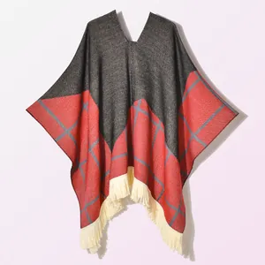 Detail of knit cape featuring red plaid pattern with ivory tassel fringe edges