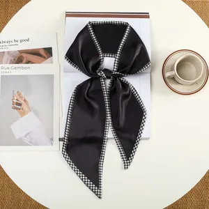Detail van zwarte satijnen sjaal met houndstooth-rand geknoopt als strik op een wit bureau