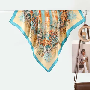 Floral print silk square scarf with blue border draped on a rack with fashion accessories
