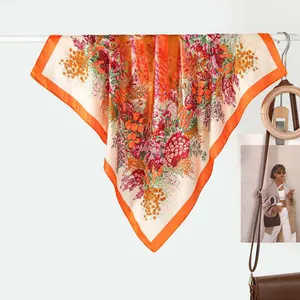 Elegant floral print silk square scarf with vibrant orange border on display hanger