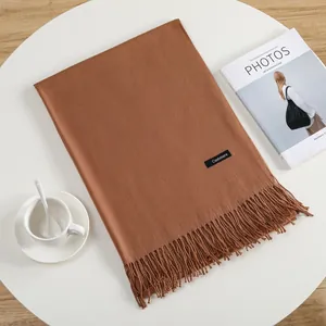 Caramel cashmere scarf with tassels styled on a white table with a coffee cup
