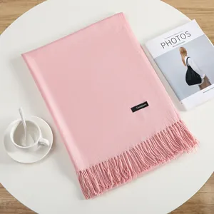 Soft pink cashmere-style winter shawl with fringe tassels on a minimalist table