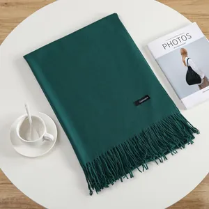 Close-up of dark green cashmere scarf with fringe details on a minimalist table