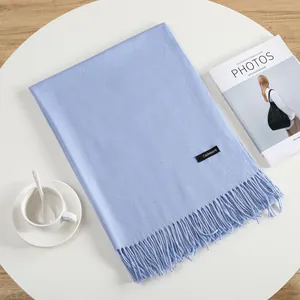 Elegant light blue cashmere scarf with tassels and stitched label on a white table