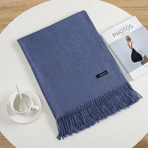 Detail of blue cashmere feel scarf with fringe trim and brand tag on a white table