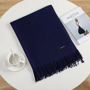 Detail shot of navy blue cashmere scarf with fringe on a white table with magazine