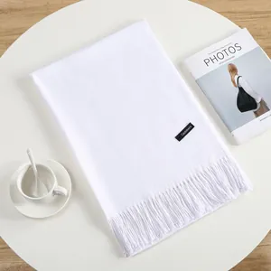 Close-up of white cashmere scarf with fringe details and woven brand label on white desk