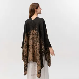 Close-up of dual-tone knit poncho featuring black abstract prints and split hem detail