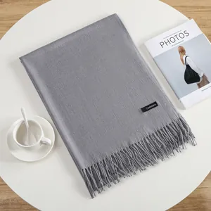 Detail of grey cashmere-like scarf with tassels and material label on a white table