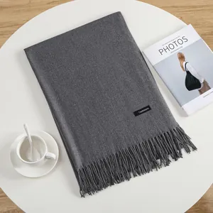 Detailed view of grey cashmere scarf with elegant tassels on a white minimalist desk