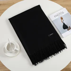 Detail of black cashmere scarf with tassels and brand label on a minimalist white table