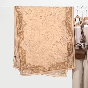 Detail view of beige linen scarf with brown paisley print hanging on a white hanger
