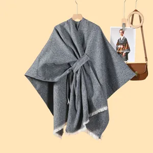 Detail eines grauen Textil-Ponchos mit weißen Fransen am Holz-Kleiderbügel hängend