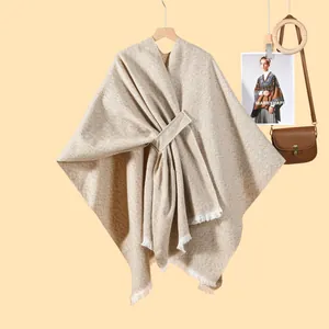 Detail eines beige gestrickten Ponchos mit Taillengürtel und weißem Quastensaum