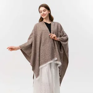 Detailaufnahme des gestrickten braunen Melange-Ponchos mit stilvollen weißen Fransen am Saum