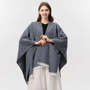 Detail eines blau-grau gestrickten Ponchos mit weißen Fransen und feiner Textur