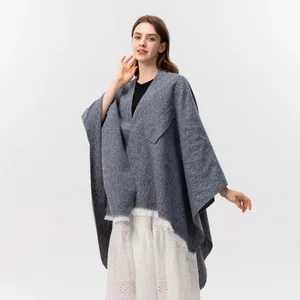 Nahaufnahme des graublauen Strickponchos mit Schrägwebstruktur und Fransenakzent
