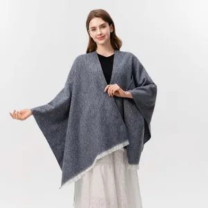 Detail des blaugrauen Strickponchos mit Fransenquasten und weicher Melange-Struktur