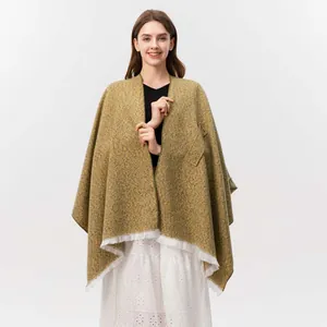 Nahaufnahme des senfgelben Strickponchos mit strukturierter Optik und weißen Fransen