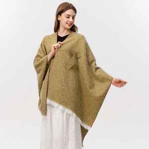 Detail der Stricktextur des senfgelben Ponchos mit Seitentasche und Fransen