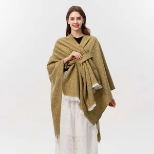 Detail eines senfgrünen Strickponchos mit weißen Fransen und Bindeband-Design