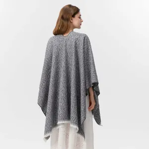 Nahaufnahme des grauen Strickponchos mit weißen Fransen und dickem strukturiertem Stoff