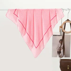 Dettaglio di un foulard di seta rosa a pois accanto a una borsa di pelle e una rivista trendy