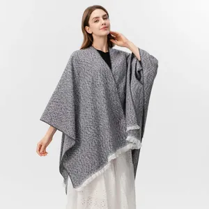 Detail eines grauen Strickschals mit gesprenkeltem Muster und weißen Fransen am Saum