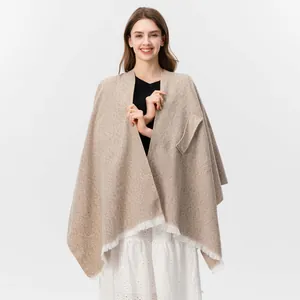 Detail der Stricktextur und weißen Fransenquasten an einem beigen Damen-Poncho