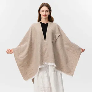 Detail eines beige gestrickten Ponchos mit aufgesetzter Tasche und weißen Fransen