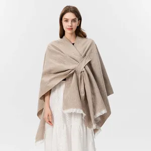 Detail eines beigen Strickschals mit Kreuzbindeverschluss und weißen Fransen am Saum