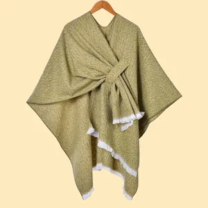 Detail eines Tweed-Ponchos in Senfgelb und Dunkelgrün mit Fransen und gekreuztem Gurt