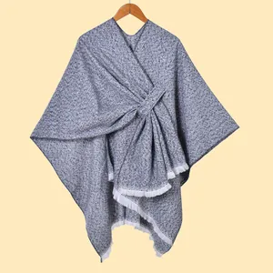 Detail eines grauen Tweed-Ponchos mit weißen Quasten, Stofftextur und Fransen