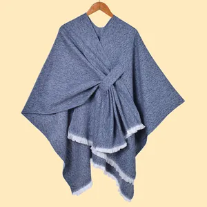 Detaillierte Strickstruktur eines Wickel-Schals mit weißen Fransen und blauem Stoff